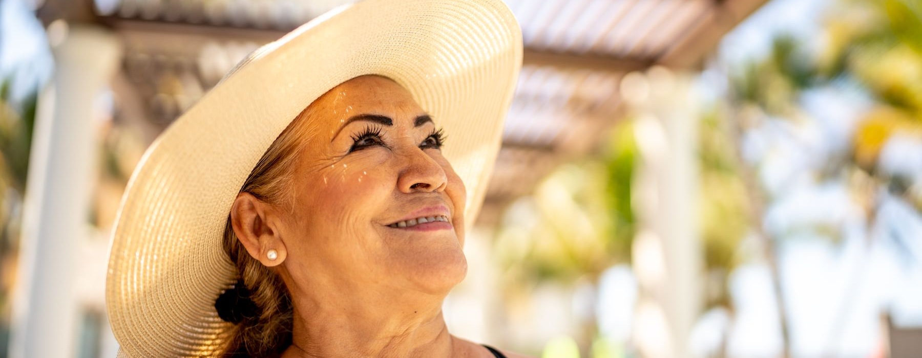 a woman outside wearing a sunhat and smiling with trees in the background